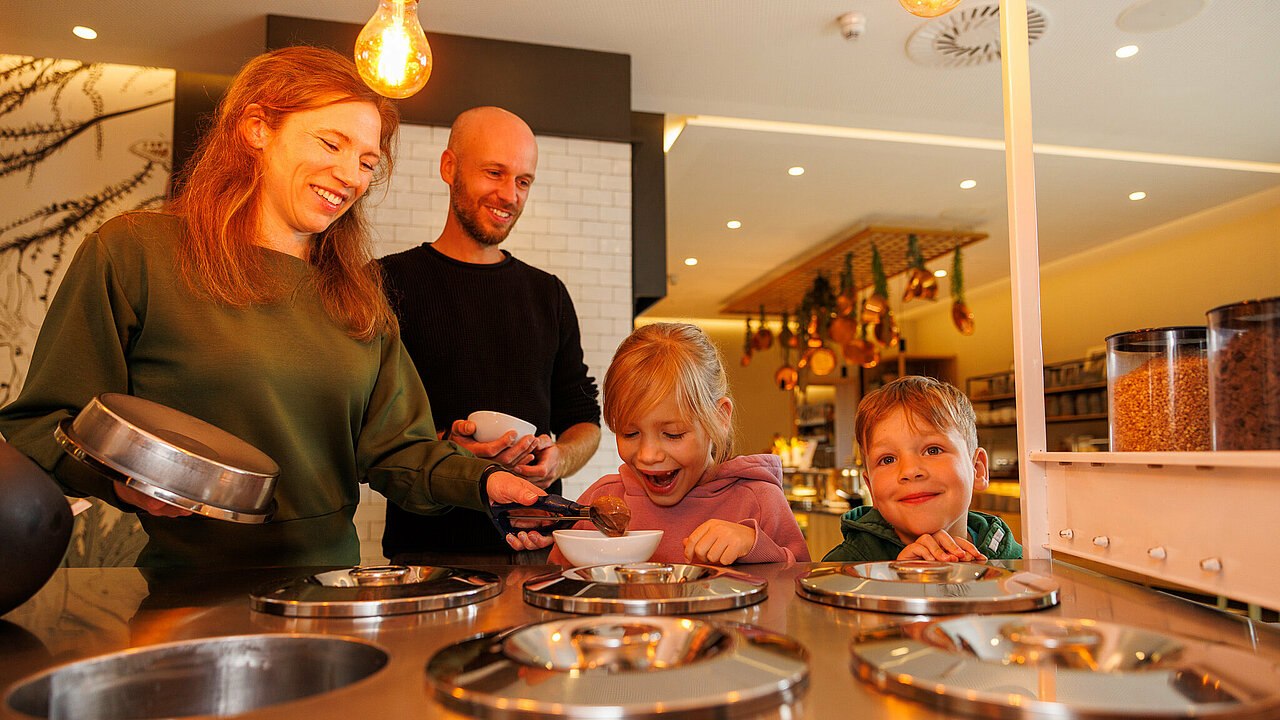 Eine freudestrahlende Familie am Eiswagen mit hausgemachten Eissorten im modernen Familienrestaurant des Elldus Resort.