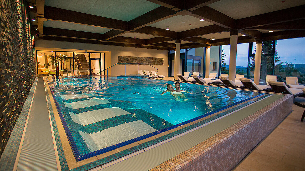 Ein Pärchen schwimmt im Elldus Spa Relaxbecken mit Unterwasserliegen.