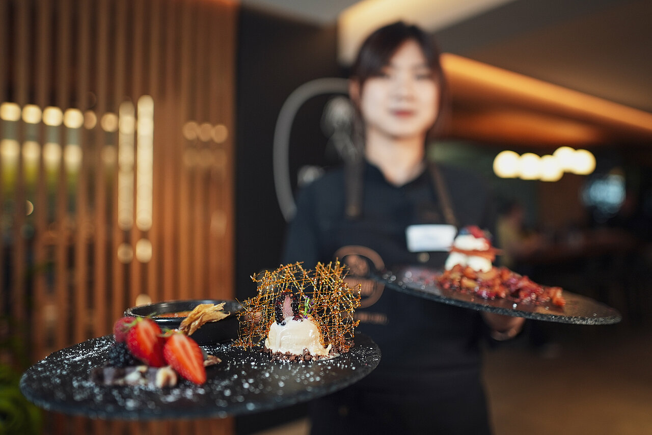 Genussrestaurant mamazita Oberwiesenthal Eine freundliche Servicemitarbeiterin präsentiert im stilvollem Ambiente des Genussrestaurants mamazita zwei hochwertig angerichtete Desserts.