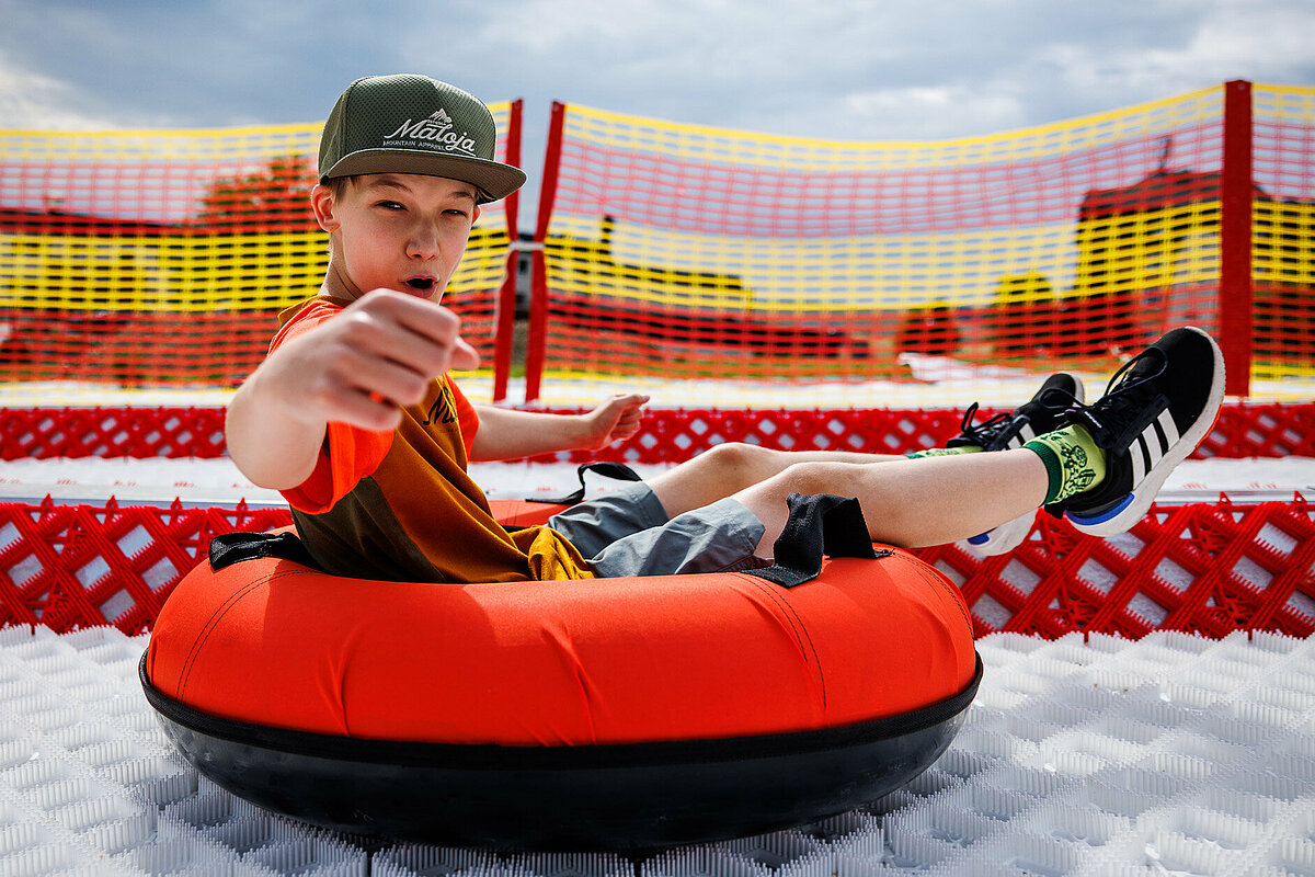 Ein Teenager sitzt in einem Gummi-Tubingring und rast cool und freudig die Tubingbahn hinunter!